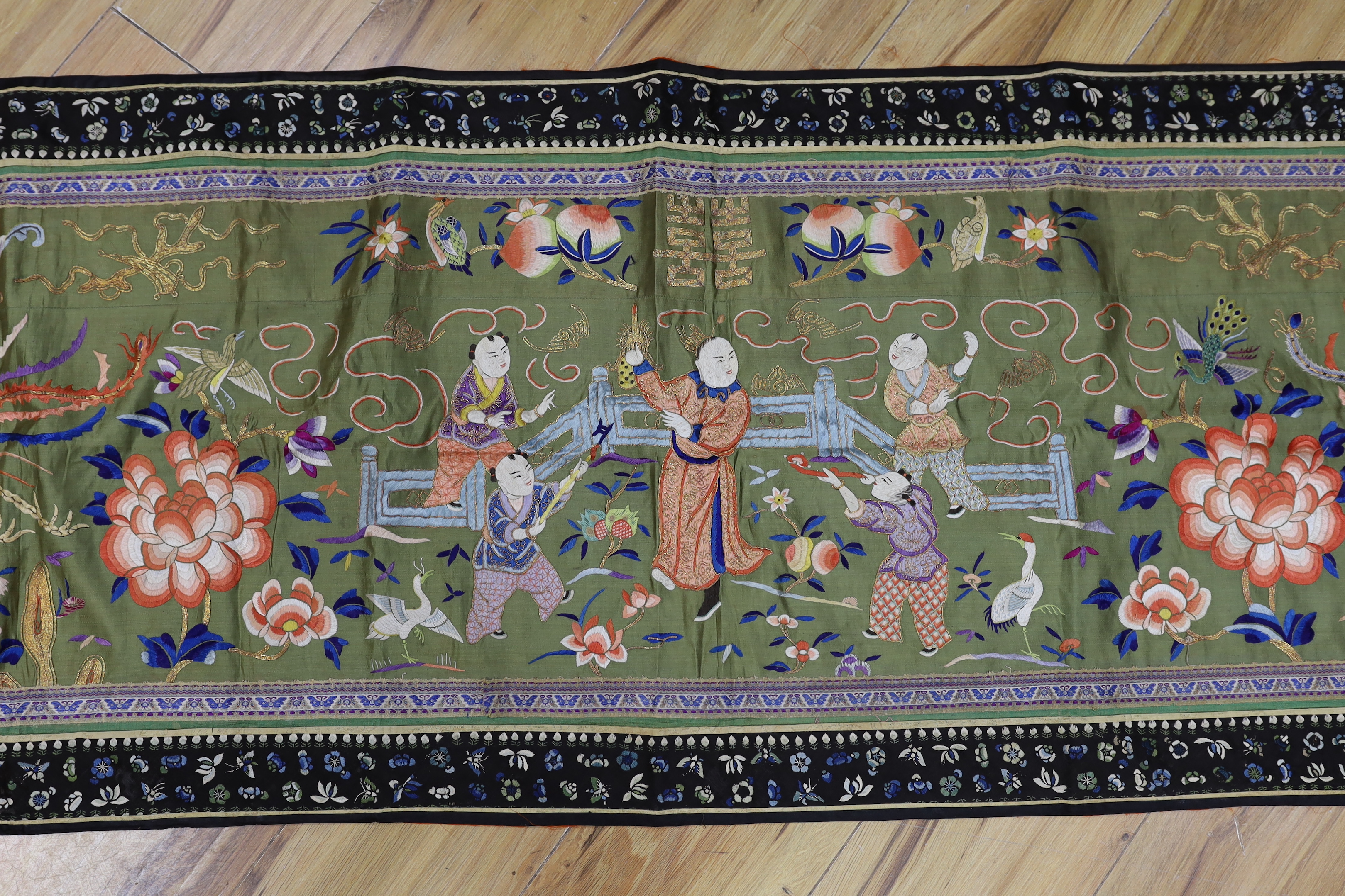 A long Chinese silk embroidered runner embroidered with the figure of Fu and boys, symbolic peaches, phoenix and flowers, possibly an altar cloth together with two other smaller runners, largest runner 202cm long x 55cm